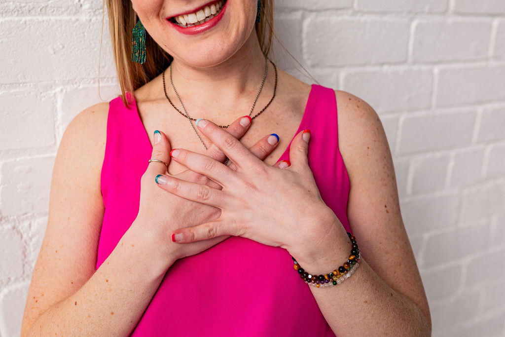 Close-up of Lindsey Hall smiling with both hands on her heart, wearing bright pink and rainbow nail polish – symbolising self-trust, emotional healing, and joy after divorce.