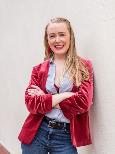 Lindsey Hall smiling confidently in a red velvet blazer, standing with arms crossed against a light wall – Divorce and Intimacy Coach based in Sheffield, England.