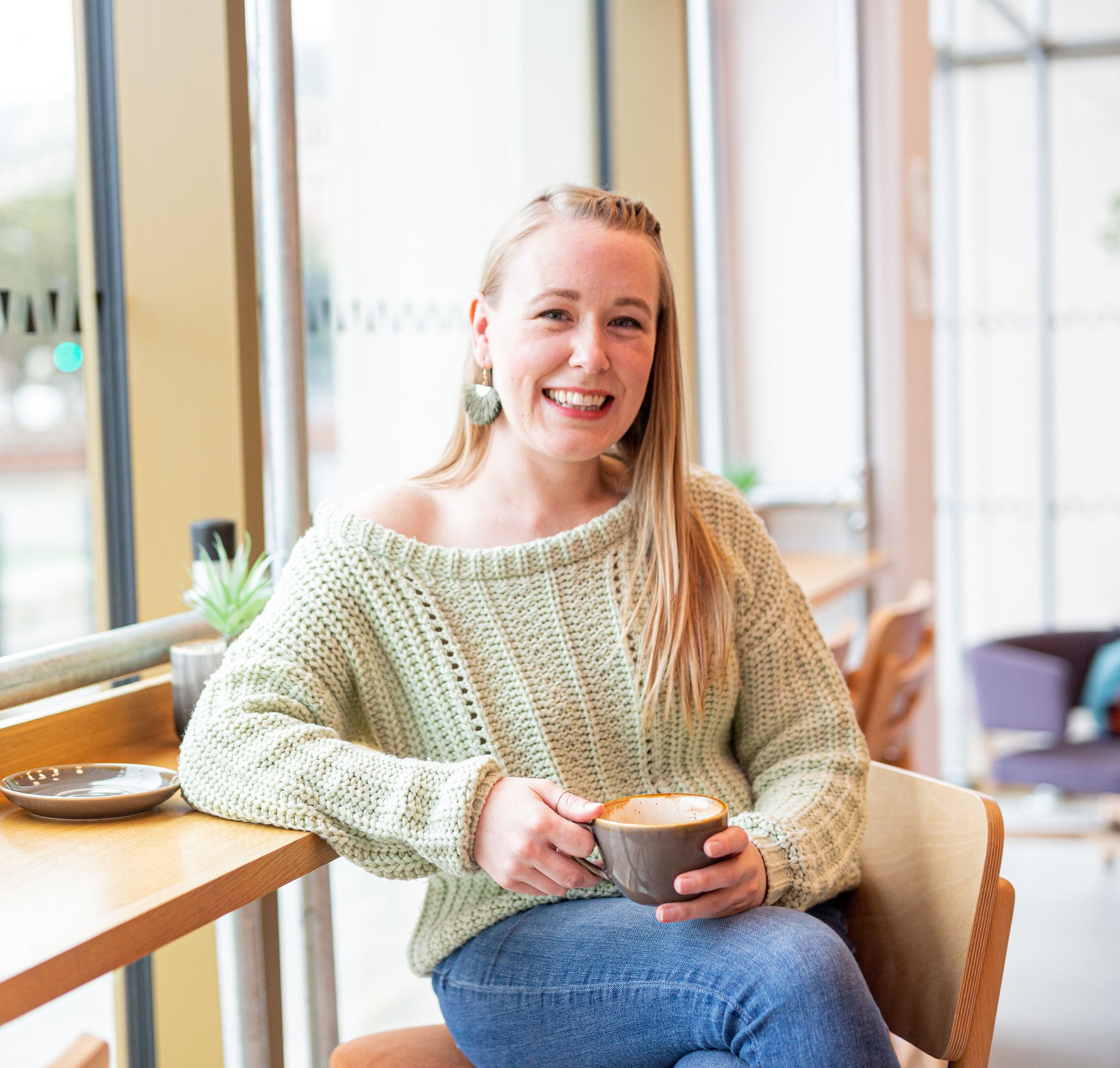 Lindsey Hall smiling warmly in a café, holding a coffee, wearing a soft green jumper. offering a grounded, approachable welcome to parents navigating divorce or separation.